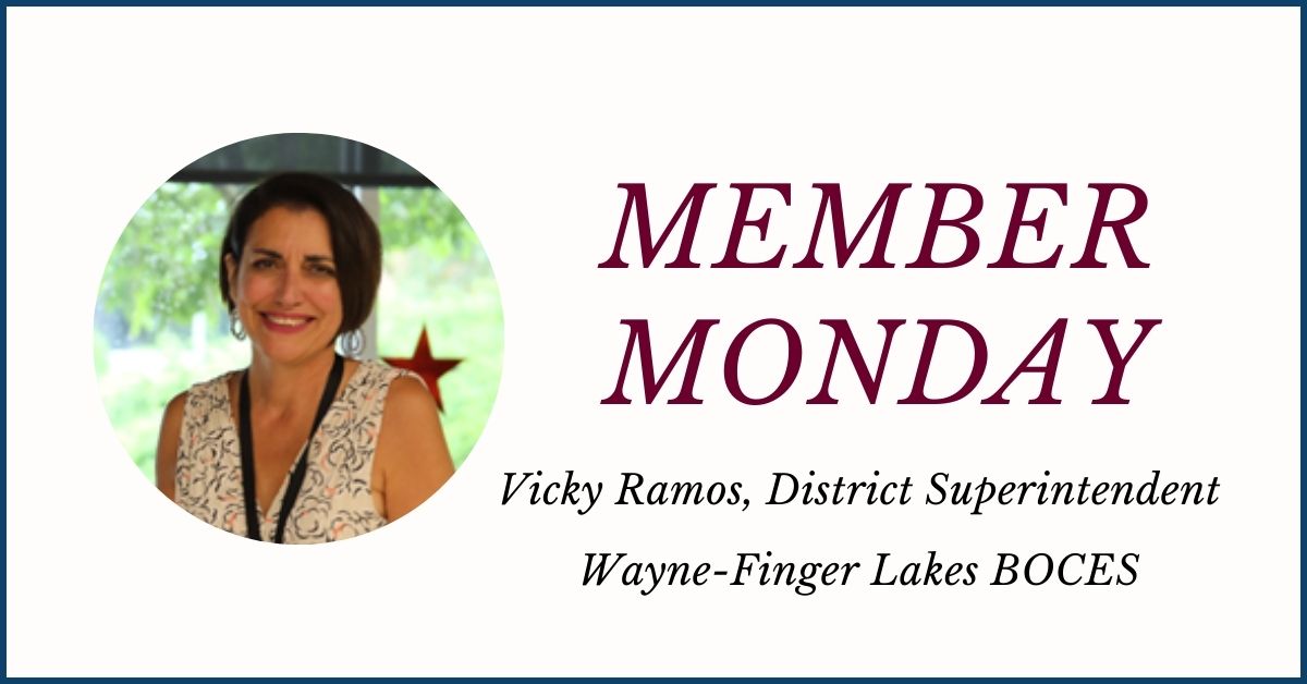 An icon featuring a circular photo at left of Vicma (Vicky) Ramos, who has short brown hair, is wearing a white and black patterned top and is looking at and smiling for the camera. The words “Member Monday Vicky Ramos, District Superintendent, Wayne-Finger Lakes BOCES” are displayed at the right.