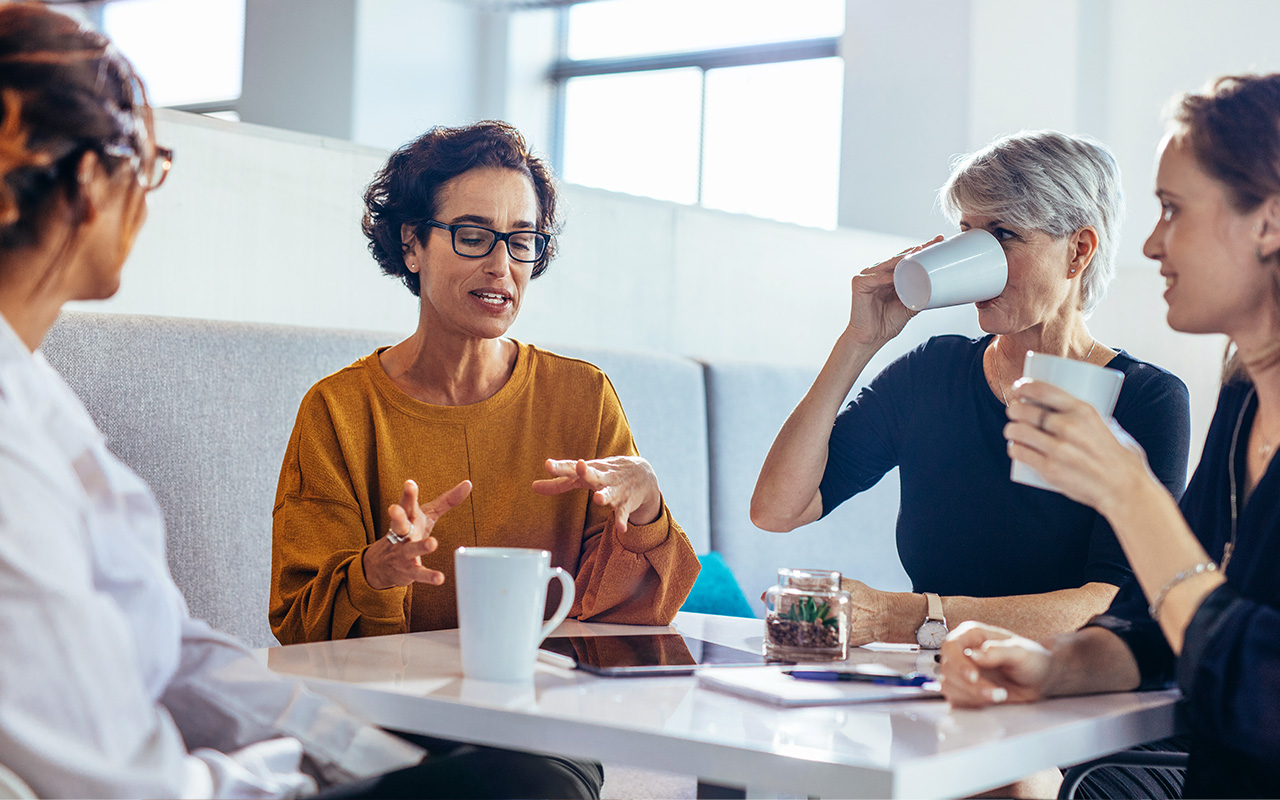 Group of four women in conversation at a table, drinking coffee