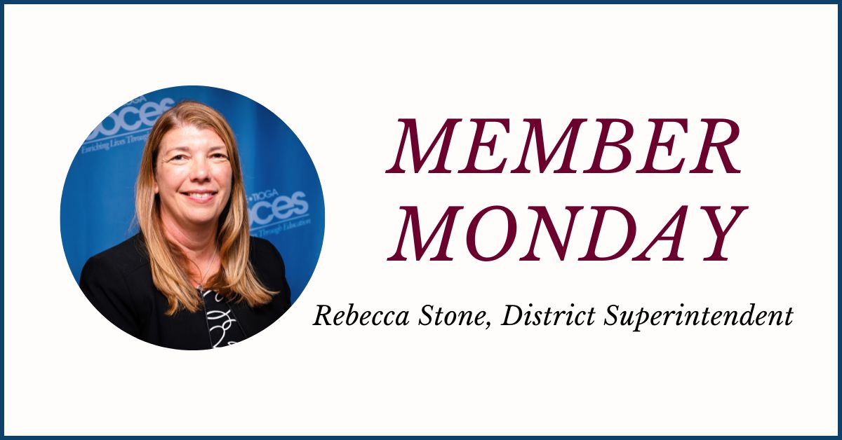 An icon featuring a circular photo at left of Rebecca Stone, who has long blond hair, is wearing a dark printed blouse and black jacket and stands in front of a bright blue background and is looking at and smiling for the camera. The words Member Monday Rebecca Stone District Superintendent are displayed at the right.
